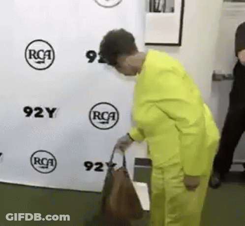 A Woman In A Yellow Suit Is Standing In Front Of A Wall That Says 92Y GIF