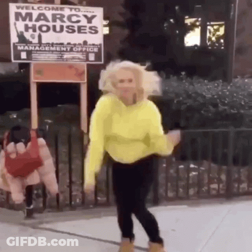 A Woman In A Yellow Sweater Is Dancing In Front Of A Marcy Houses Sign . GIF