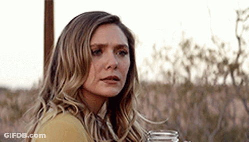 A Woman In A Yellow Sweater Is Holding A Mason Jar In A Field . GIF