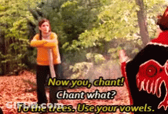 A Woman In A Yellow Sweater Is Standing Next To A Man In A Red Jacket Who Says " Now You Chant " GIF