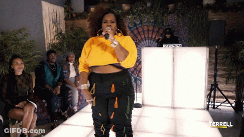 A Woman In A Yellow Sweater Sings Into A Microphone In Front Of A Dj Booth That Says Terrell On It GIF