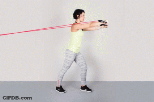 A Woman In A Yellow Tank Top Is Doing Exercises With A Resistance Band GIF
