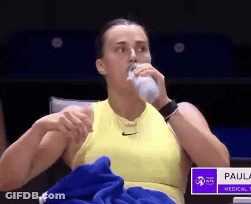 A Woman In A Yellow Tank Top Is Drinking Water From A Bottle . GIF