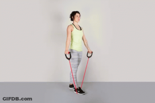 A Woman In A Yellow Tank Top Is Holding A Red Resistance Band GIF