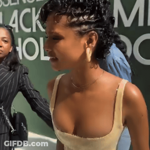 A Woman In A Yellow Tank Top Stands In Front Of A Green Wall That Says Black Hollywood GIF