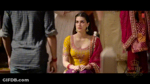 A Woman In A Yellow Top And Purple Pants Is Sitting In Front Of A Man In A Blue Shirt . GIF