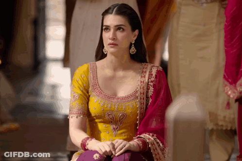 A Woman In A Yellow Top And Purple Pants Sits On A Bench GIF