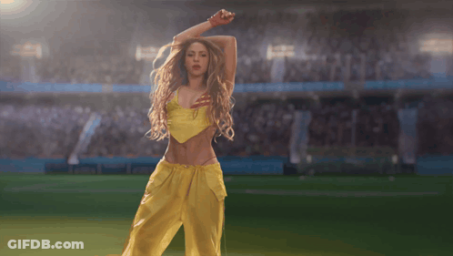 A Woman In A Yellow Top And Yellow Pants Is Dancing On A Soccer Field GIF