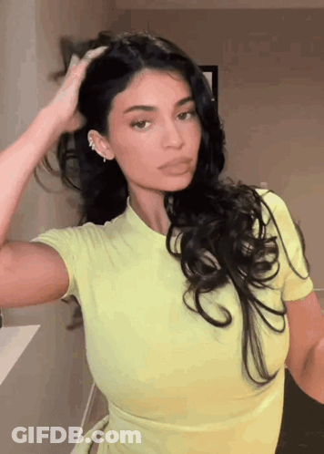 A Woman In A Yellow Top Is Holding Her Hair GIF