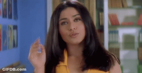 A Woman In A Yellow Top Is Standing In Front Of A Bookshelf And Smoking A Cigarette . GIF