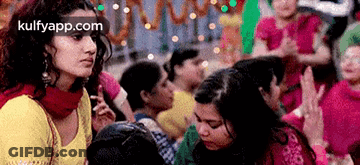 A Woman In A Yellow Top Is Standing In Front Of A Crowd Of People With The Website Kulfyapp.com In The Corner GIF