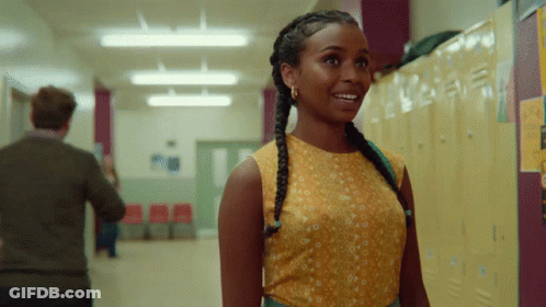 A Woman In A Yellow Top Stands In A Hallway Next To Lockers GIF