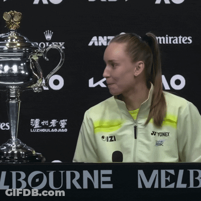 A Woman In A Yellow Yonex Jacket Stands In Front Of A Trophy At A Press Conference GIF