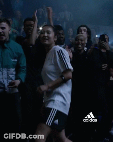 A Woman In An Adidas Shirt Is Dancing In A Crowd Of People GIF