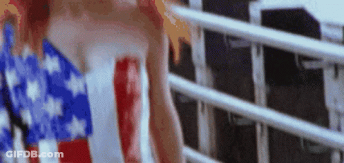A Woman In An American Flag Dress Is Standing Next To A Railing . GIF