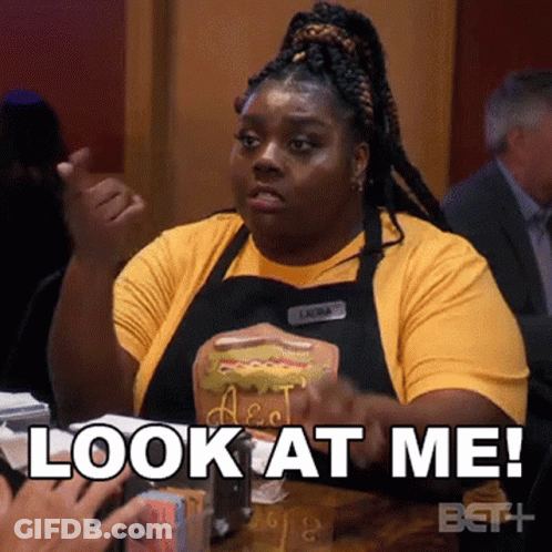 A Woman In An Apron Is Holding A Hot Dog And Says Look At Me . GIF