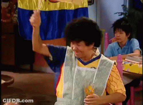 A Woman In An Apron Is Sitting At A Table With A Glass Of Orange Juice . GIF
