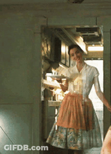 A Woman In An Apron Is Standing In A Kitchen GIF