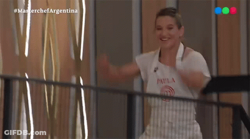 A Woman In An Apron Is Standing On A Balcony With Her Arms Outstretched And Smiling . GIF