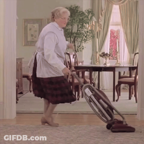 A Woman In An Apron Is Using A Vacuum Cleaner In A Dining Room GIF
