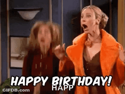 A Woman In An Orange Coat Is Standing Next To Another Woman In A Living Room . GIF