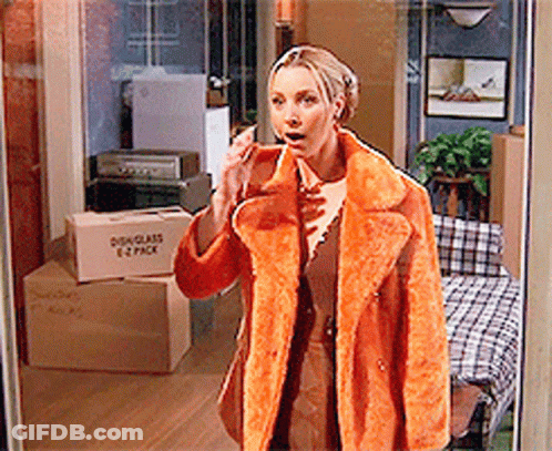 A Woman In An Orange Coat Is Talking On A Cell Phone In Front Of A Moving Box That Says 1 2 Pack GIF