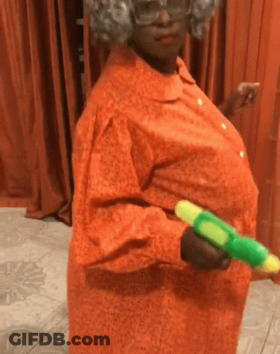A Woman In An Orange Dress Is Holding A Green Toy Water Gun GIF