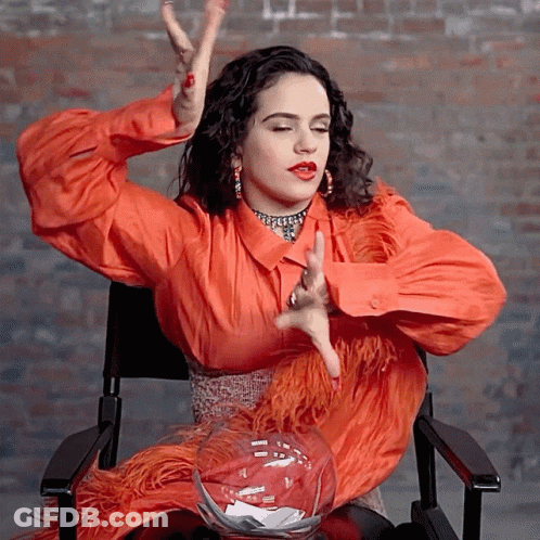 A Woman In An Orange Dress Is Sitting In A Chair GIF
