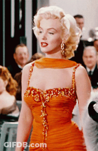 A Woman In An Orange Dress Is Standing In A Crowd GIF