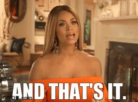 A Woman In An Orange Dress Is Standing In Front Of A Fireplace . GIF