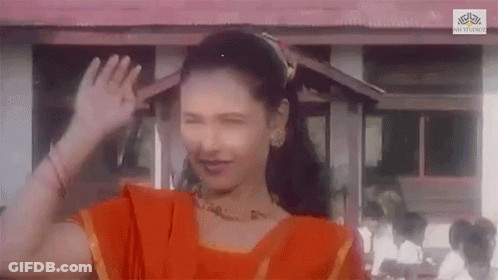 A Woman In An Orange Dress Is Waving Her Hand In Front Of A Building GIF