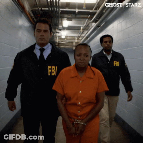 A Woman In An Orange Jumpsuit Is Being Escorted By Two Men In Fbi Uniforms GIF