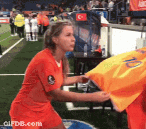 A Woman In An Orange Shirt Is Holding A Yellow Shirt With The Number 10 On It . GIF