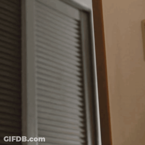 A Woman In An Orange Shirt Is Peeking Out From Behind A Wall GIF