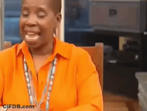 A Woman In An Orange Shirt Is Smiling And Sitting In A Chair . GIF