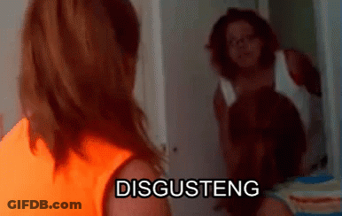 A Woman In An Orange Shirt Is Standing In Front Of A Mirror With The Word Disgusteng On It GIF