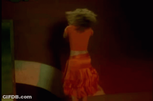 A Woman In An Orange Skirt Is Dancing In A Dark Room . GIF