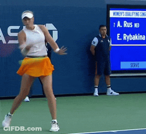 A Woman In An Orange Skirt Is Playing Tennis On A Tennis Court GIF