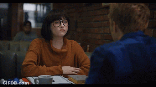 A Woman In An Orange Sweater Sits At A Table With A Man GIF