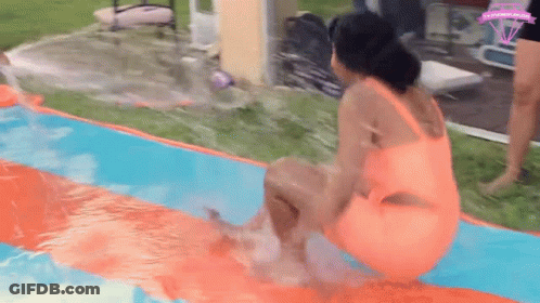 A Woman In An Orange Swimsuit Is Sitting On Top Of A Water Slide In A Pool . GIF