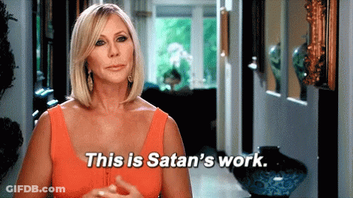 A Woman In An Orange Tank Top Is Standing In A Hallway And Saying This Is Satan 'S Work . GIF