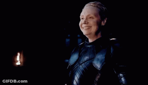 A Woman In Armor Is Smiling With Her Eyes Closed . GIF
