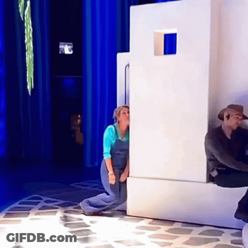 A Woman In Blue Overalls Is Peeking Out From Behind A Wall GIF