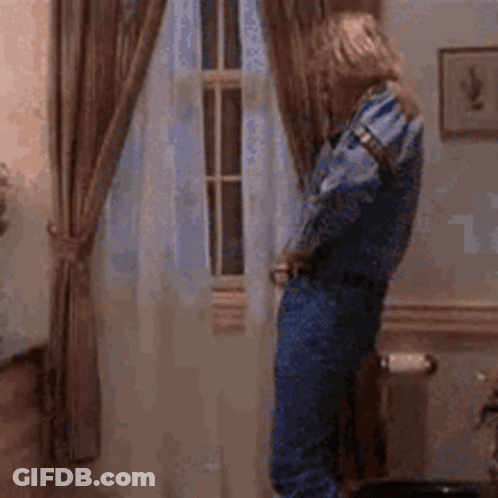 A Woman In Blue Overalls Is Standing In Front Of A Window . GIF