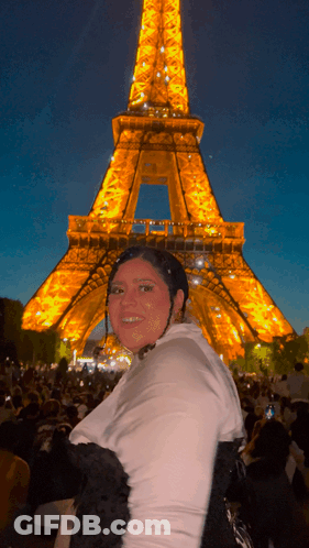 A Woman In Front Of The Eiffel Tower At Night GIF