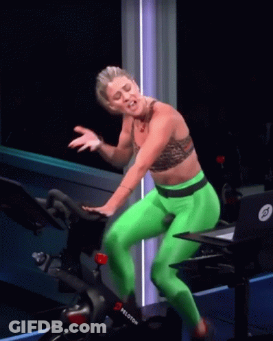 A Woman In Green Pants Is Riding A Peloton Exercise Bike GIF