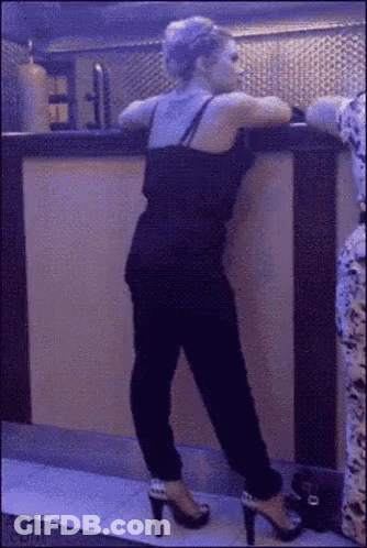 A Woman In High Heels Leans Against A Bar GIF