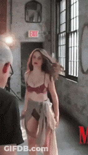 A Woman In Lingerie Is Standing In Front Of A Window With An Exit Sign Above Her GIF