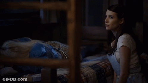 A Woman In Overalls And A White Shirt Is Standing In A Dark Room GIF