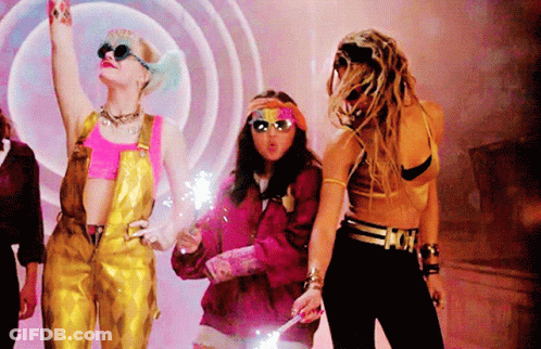 A Woman In Overalls Is Holding A Sparkler In Her Hand While Standing Next To Two Other Women GIF